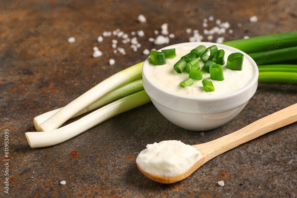 Bowl and spoon of tasty sour cream with sliced green onion on dark background