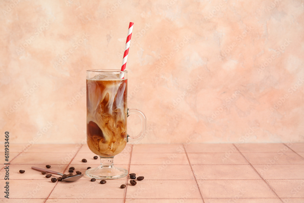 Glass of ice coffee with straw, spoon  and beans on beige tile table near wall