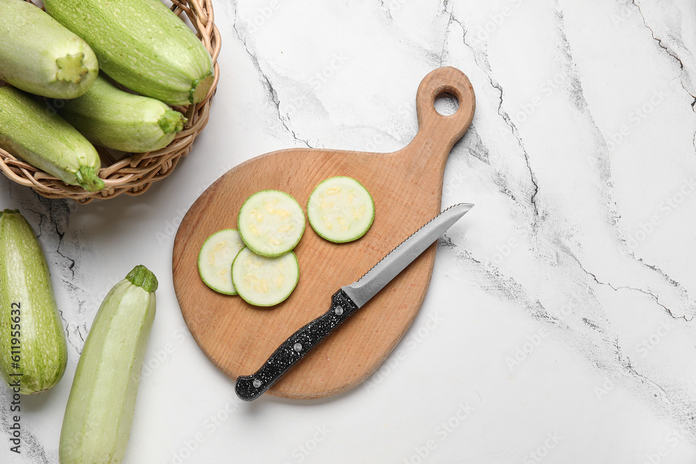 Wooden board with fresh zucchini on white marble background