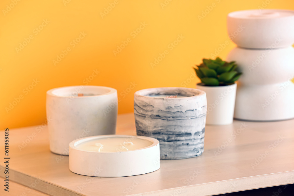 Holders with candles and houseplant on table near orange wall in room, closeup