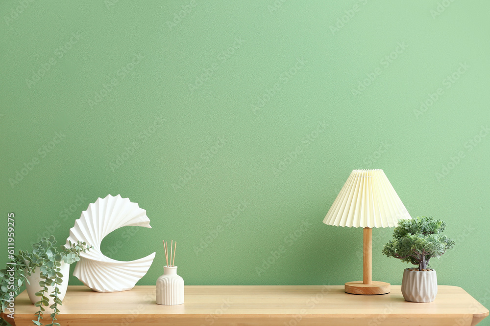 Bottle of reed diffuser, houseplants and lamp on table near color wall in room