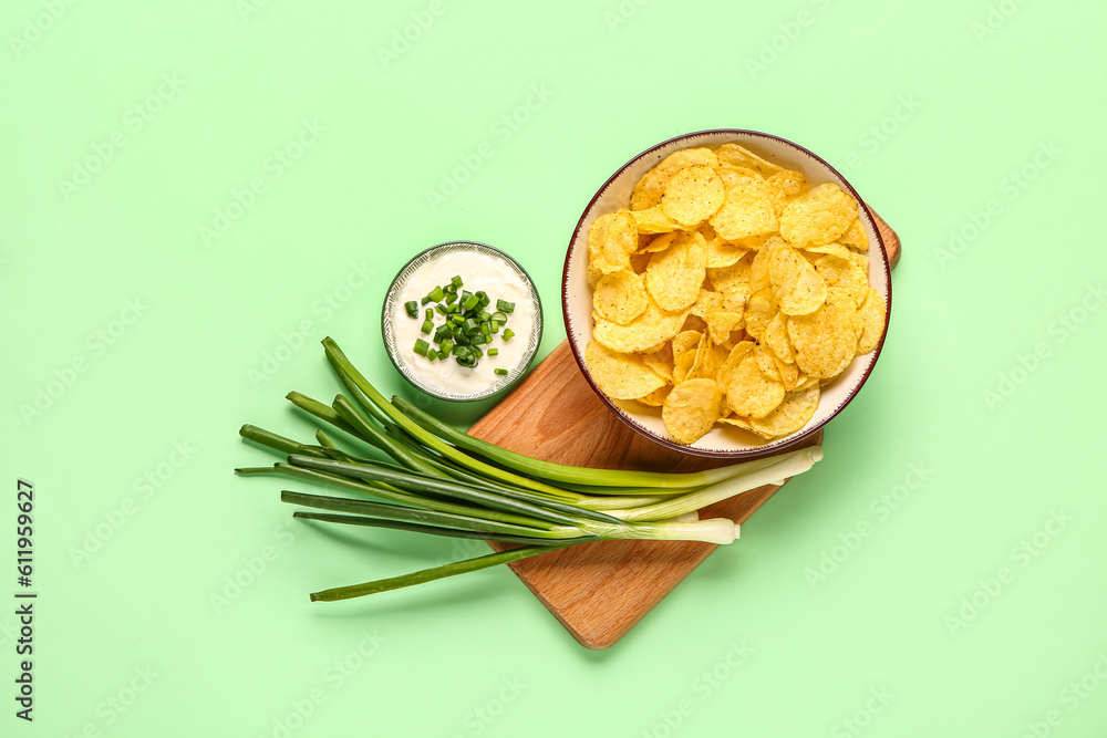 Bowl of tasty sour cream with sliced scallion and potato chips on green background