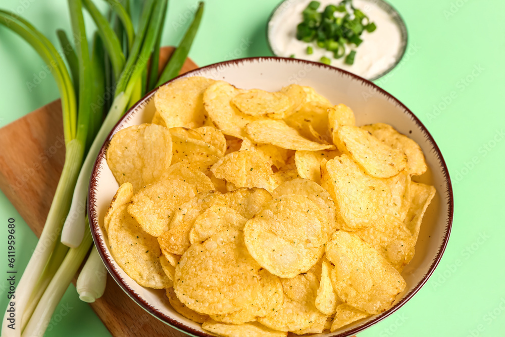 Bowl of tasty sour cream with sliced scallion and potato chips on green background