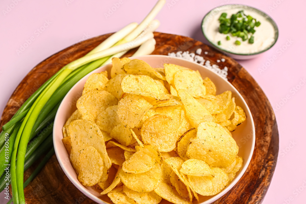 Bowl of tasty sour cream with sliced green onion and potato chips on lilac background