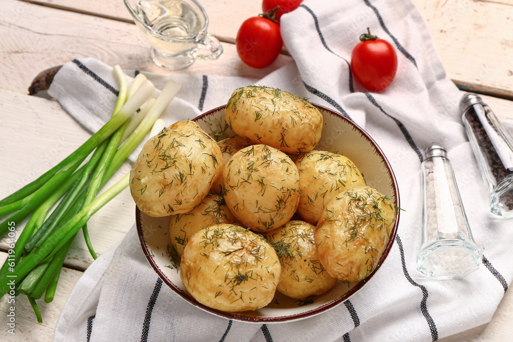 Plate of boiled baby potatoes with dill and tomatoes on white wooden background