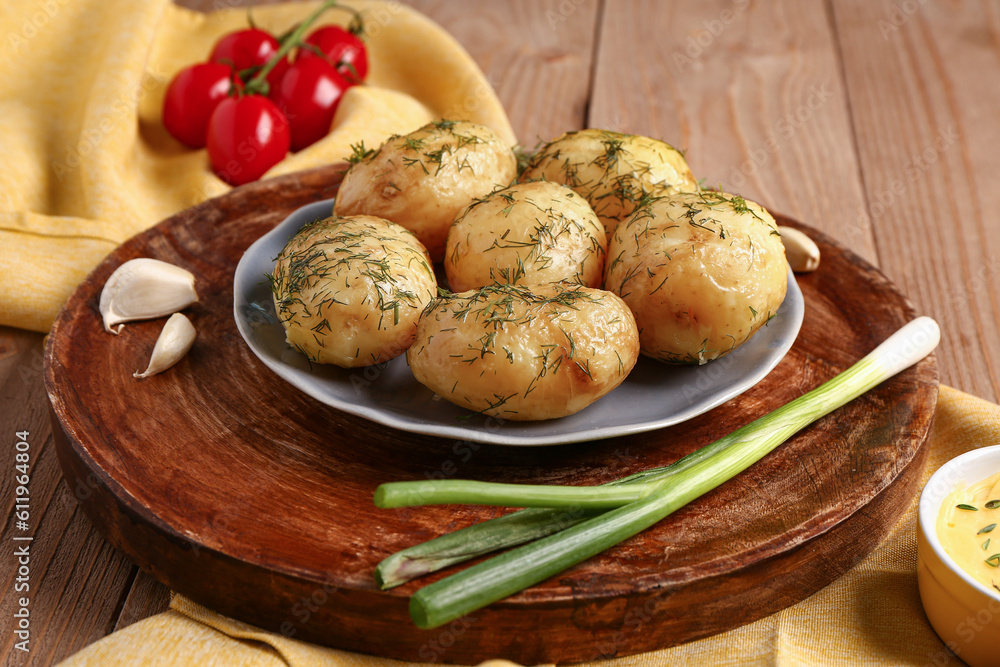 Plate of boiled baby potatoes with dill and green onion on wooden background