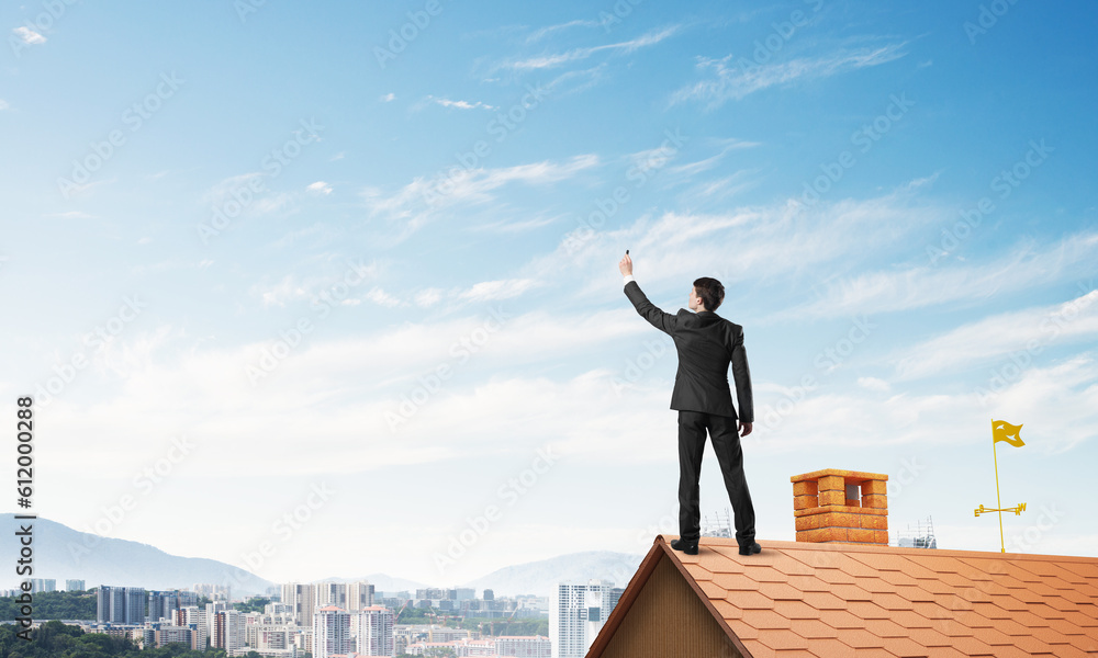 Businessman on house roof touch empty space. Mixed media