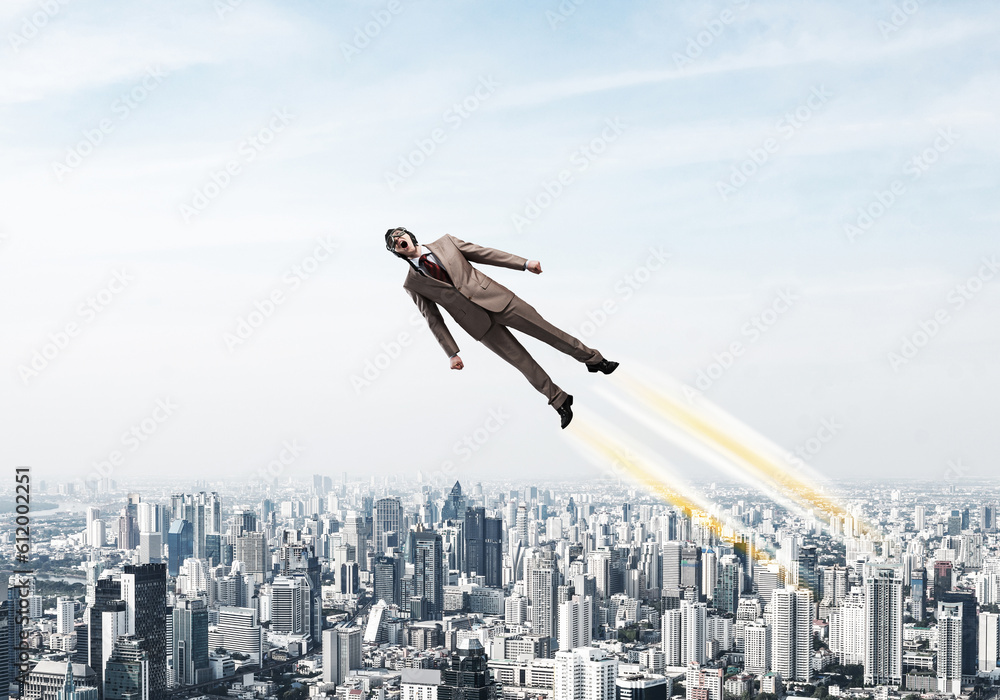 Businessman in suit and aviator hat flying in sky