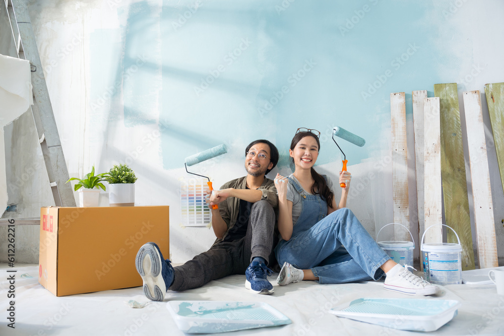 Portrait Asian couple repairing and painting the wall with blue paint using a roller during renovati