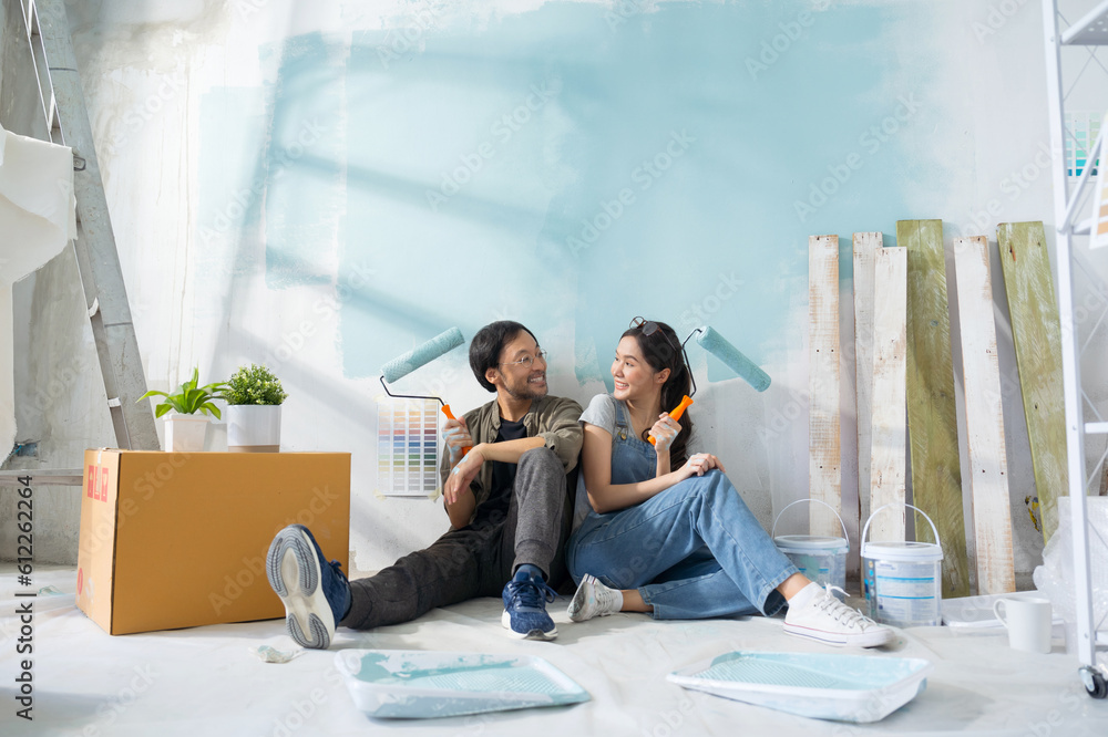 Portrait Asian couple repairing and painting the wall with blue paint using a roller during renovati