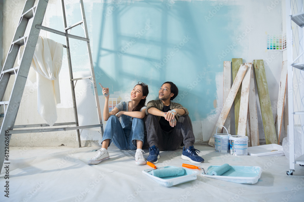 Asian couple talking chatting while taking a break from painting the walls of their house.