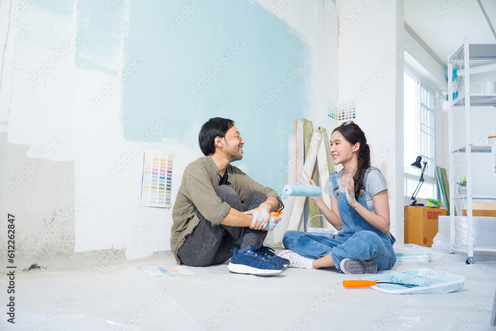 Asian couple talking chatting while taking a break from painting the walls of their house.