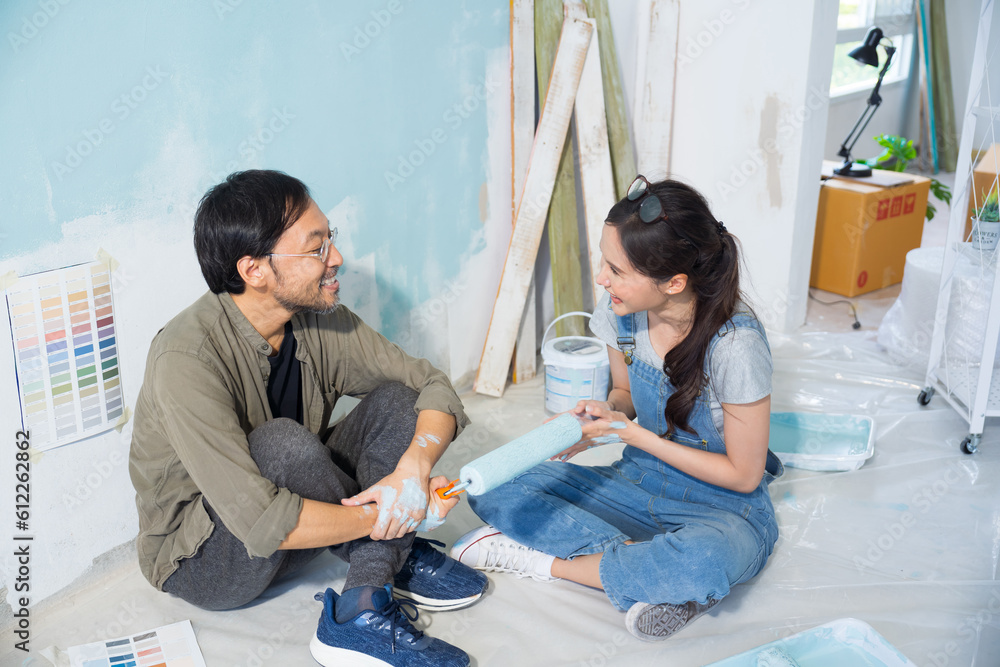 Asian couple talking chatting while taking a break from painting the walls of their house.