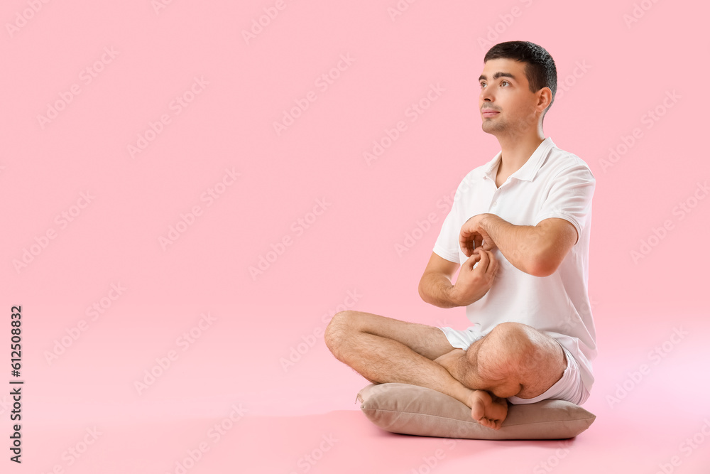 Young man meditating on pink background