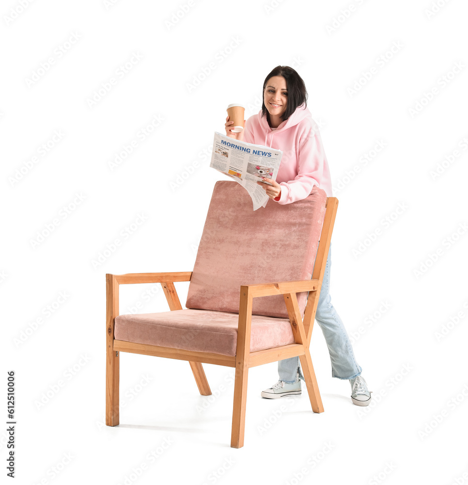 Beautiful woman with cup of coffee and newspaper beside pink armchair on white background