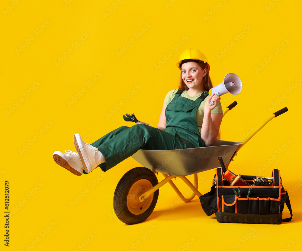 Female builder with megaphone sitting in wheelbarrow on yellow background