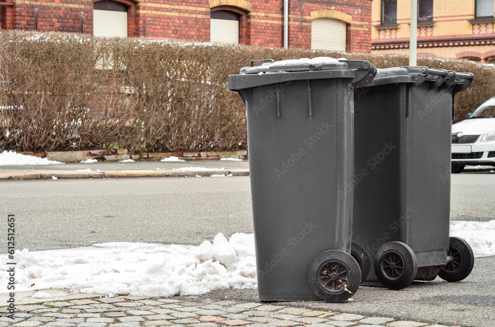 View of black garbage containers in city on winter day