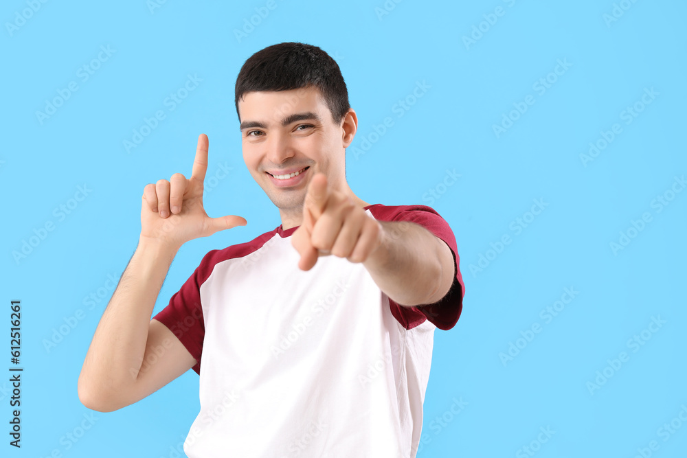 Young man showing loser gesture on blue background