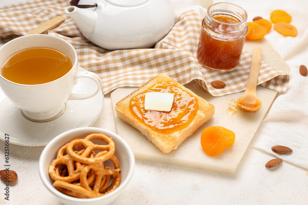 Tasty toast with apricot jam, cookies and cup of tea on light background