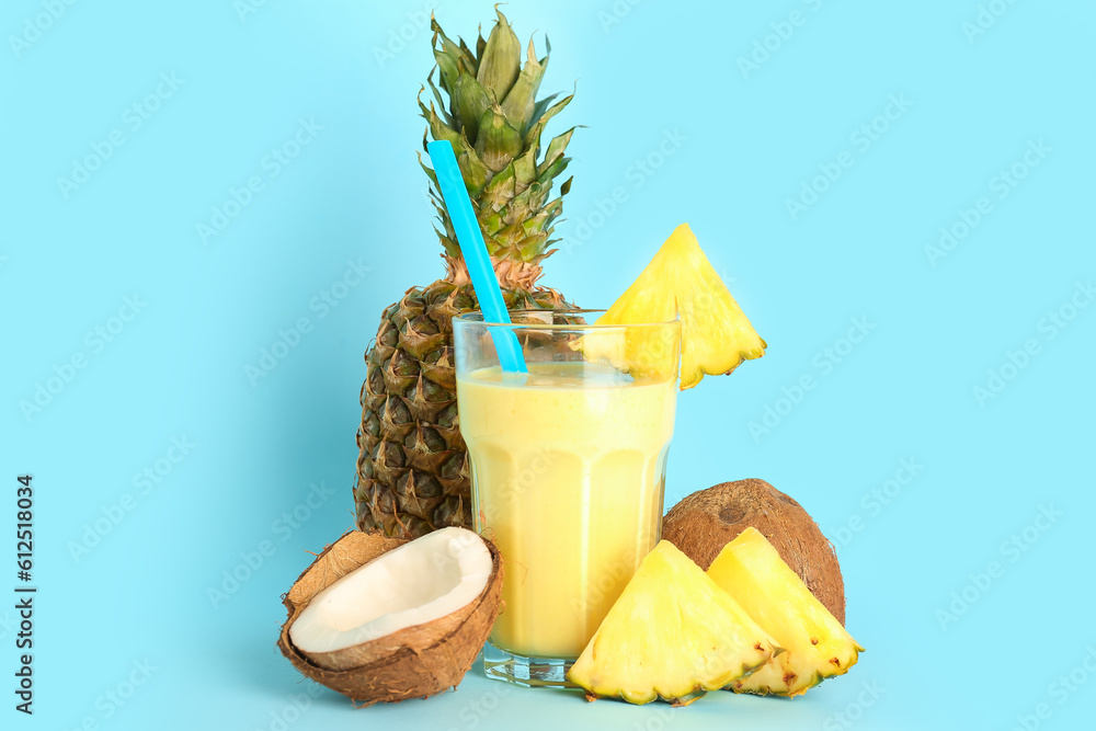 Glass of tasty pineapple smoothie, straw and coconut on blue background