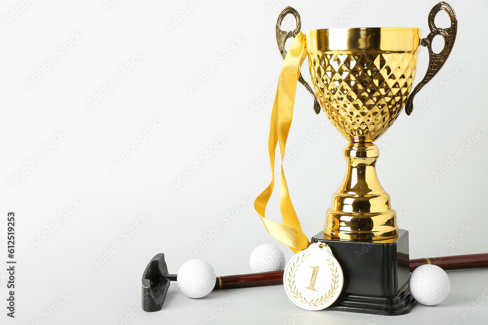 Gold cup with first place medal, golf club and balls on light background