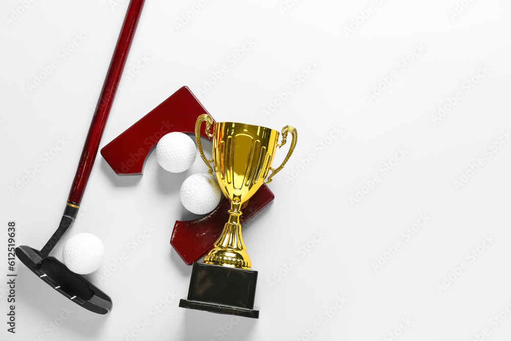 Gold cup with golf club and balls on light background