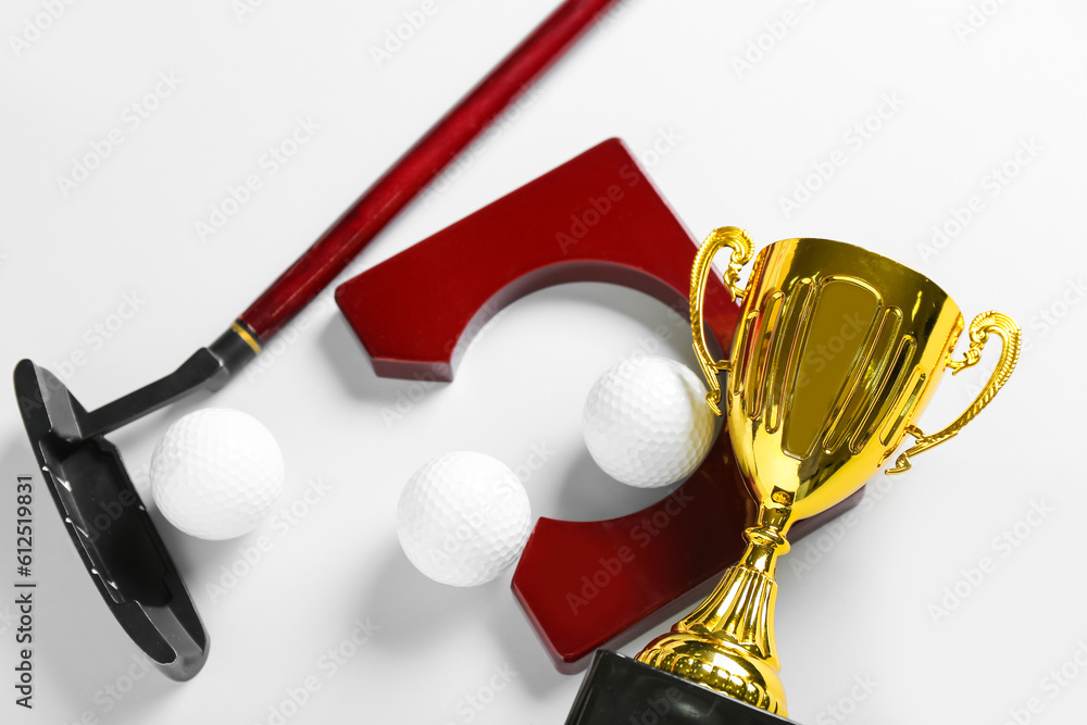 Gold cup with golf club and balls on light background