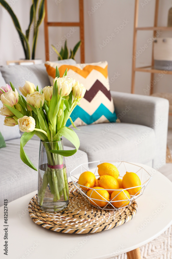 Vase with beautiful tulip flowers and lemons on coffee table in interior of living room