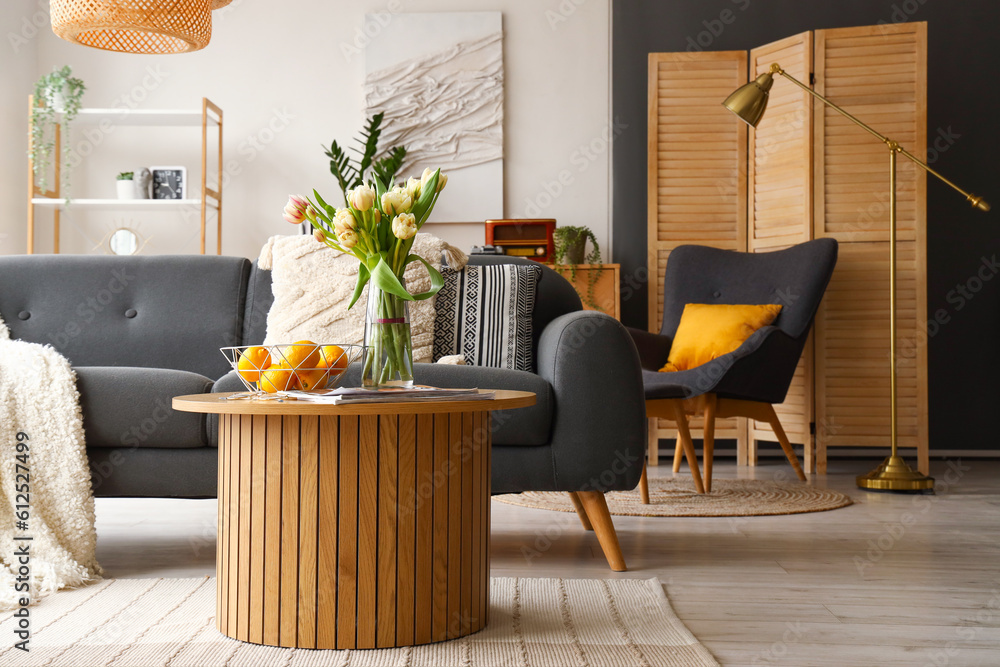 Vase with tulip flowers, lemons and magazines on coffee table in interior of living room