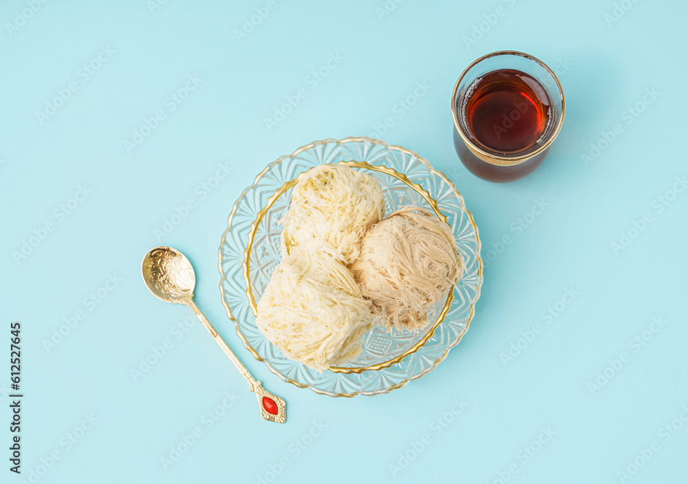 Bowls with tasty Turkish Pismaniye and glass of tea on blue background