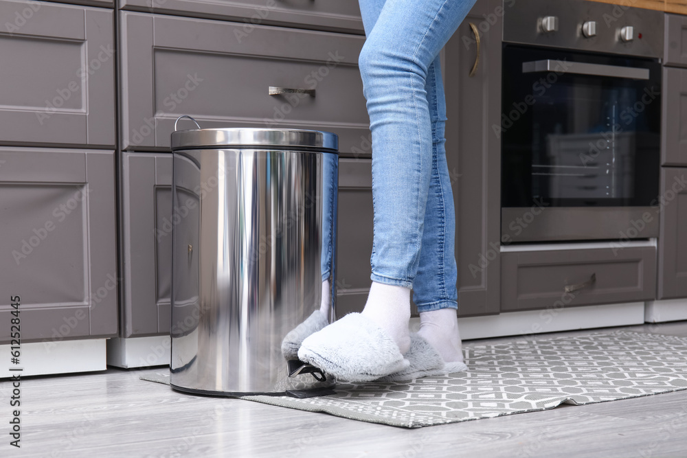 Woman opening trash been with her foot in modern kitchen