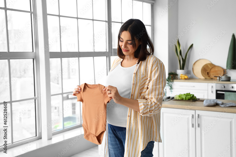 Young pregnant woman with baby bodysuit in kitchen