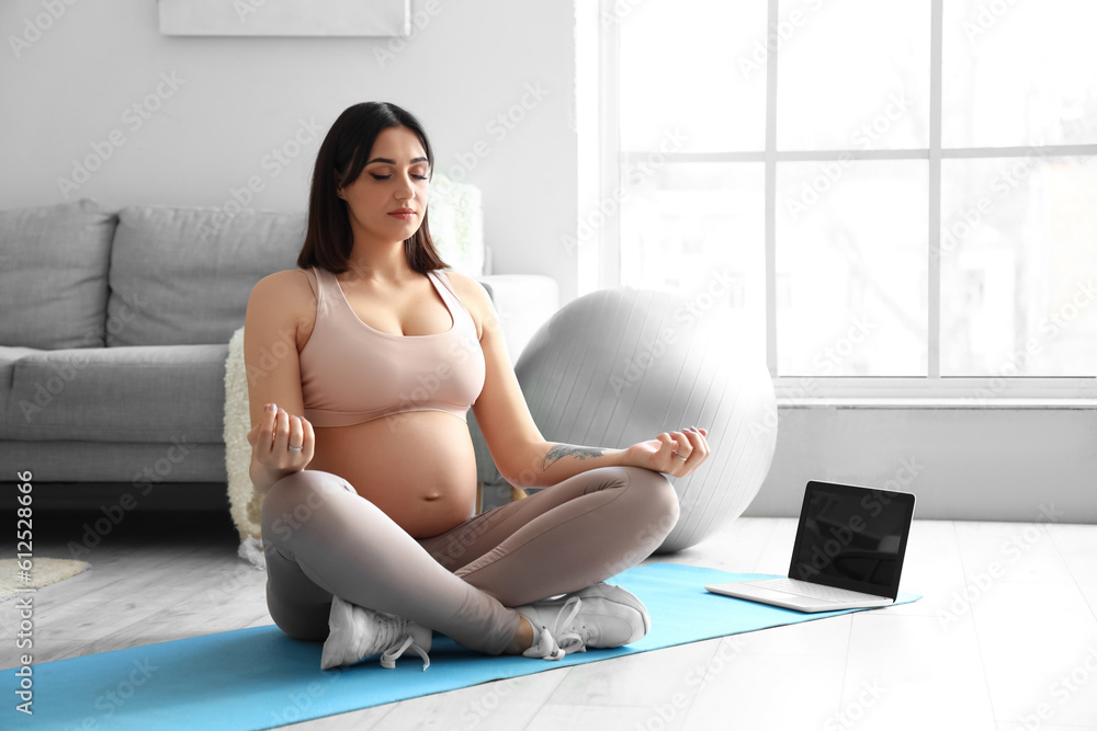 Sporty young pregnant woman meditating at home