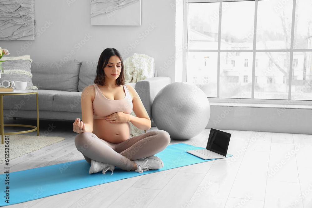 Sporty young pregnant woman meditating at home