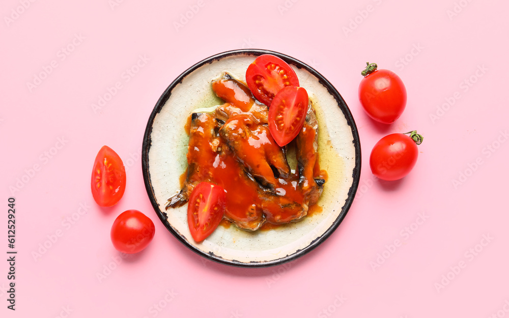 Plate with canned fish in sauce and tomatoes on pink background