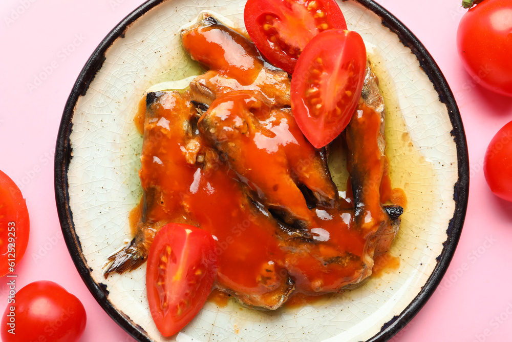 Plate with canned fish in sauce and tomatoes on pink background