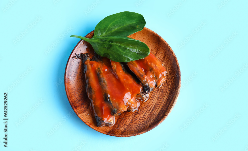 Plate with canned fish in tomato sauce and spinach leaves on blue background