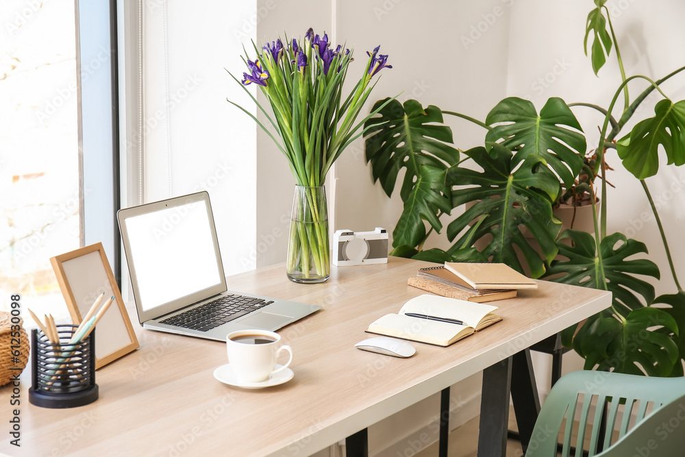 Modern workplace with laptop, notebooks, coffee cup and flowers in office