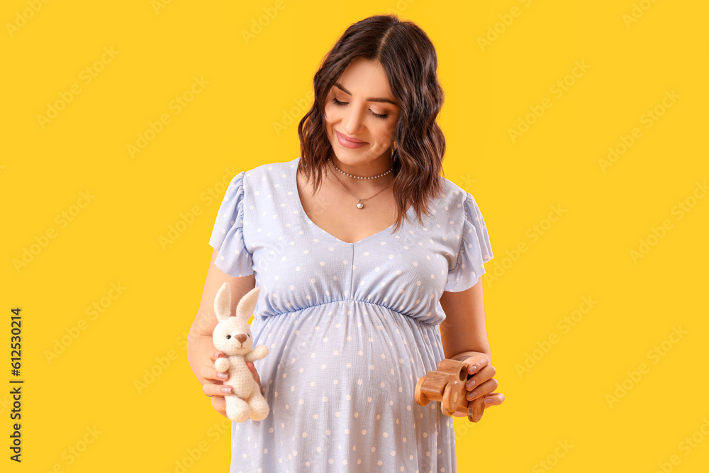 Young pregnant woman with baby toys on yellow background