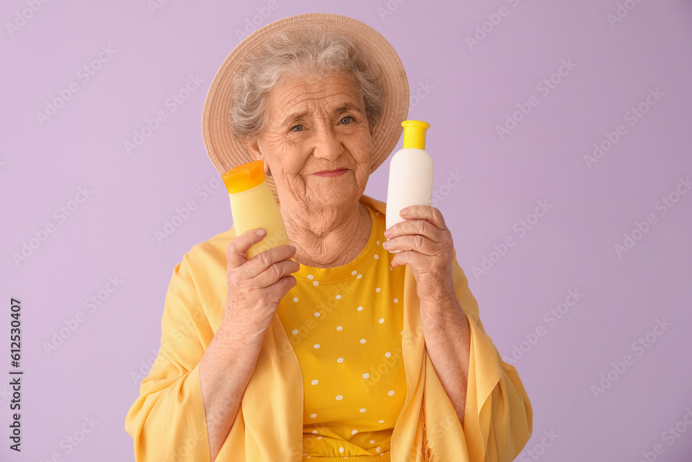 Senior woman with bottles of sunscreen cream on lilac background