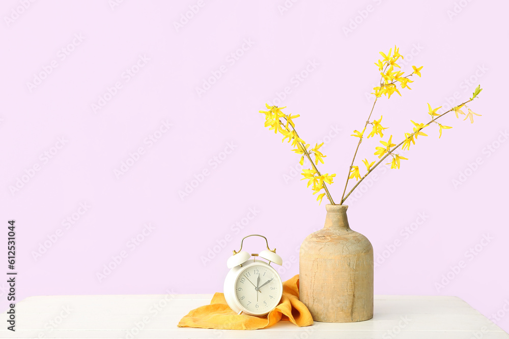 Vase with blooming tree branches and alarm clock on white table against pink background