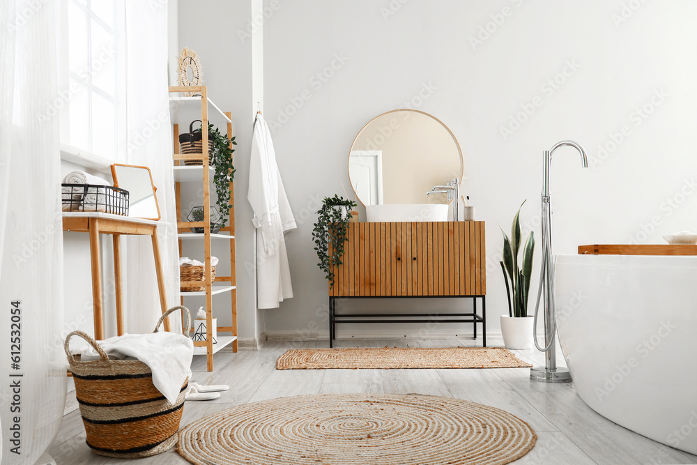 Interior of light bathroom with bathtub, wooden cabinet and mirror