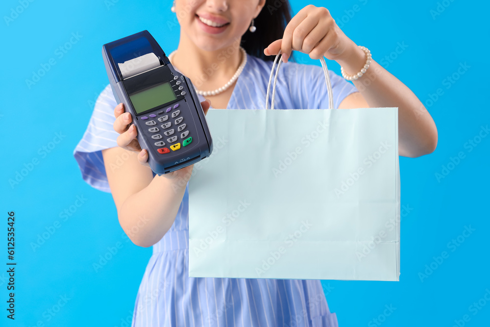 Young woman with shopping bag and payment terminal on blue background, closeup