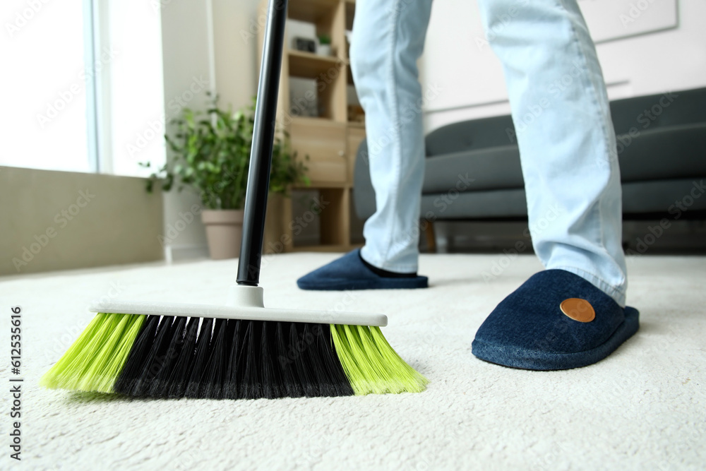 Young man sweeping carpet with broom at home, closeup