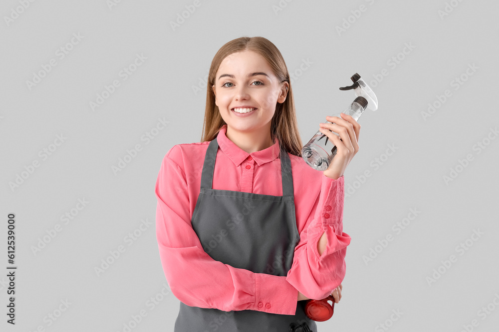 Female hairdresser with spray on grey background