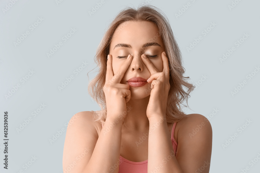 Young woman doing face building exercise on light background, closeup