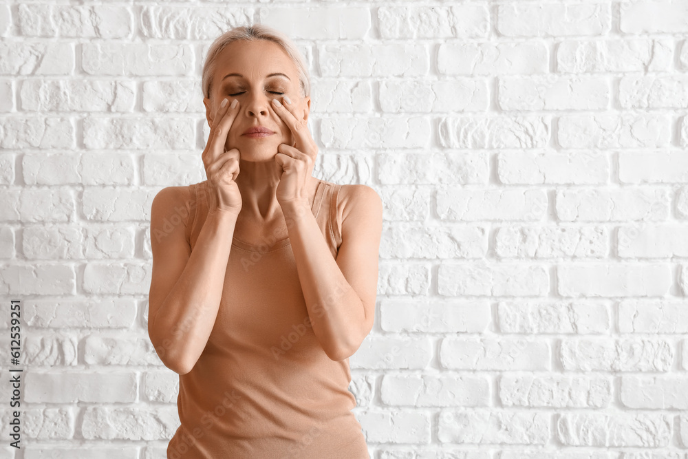 Mature woman doing face building exercise on white brick background