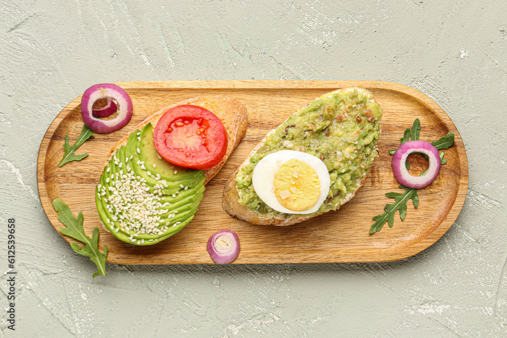 Wooden board of tasty bruschettas with avocado on light background