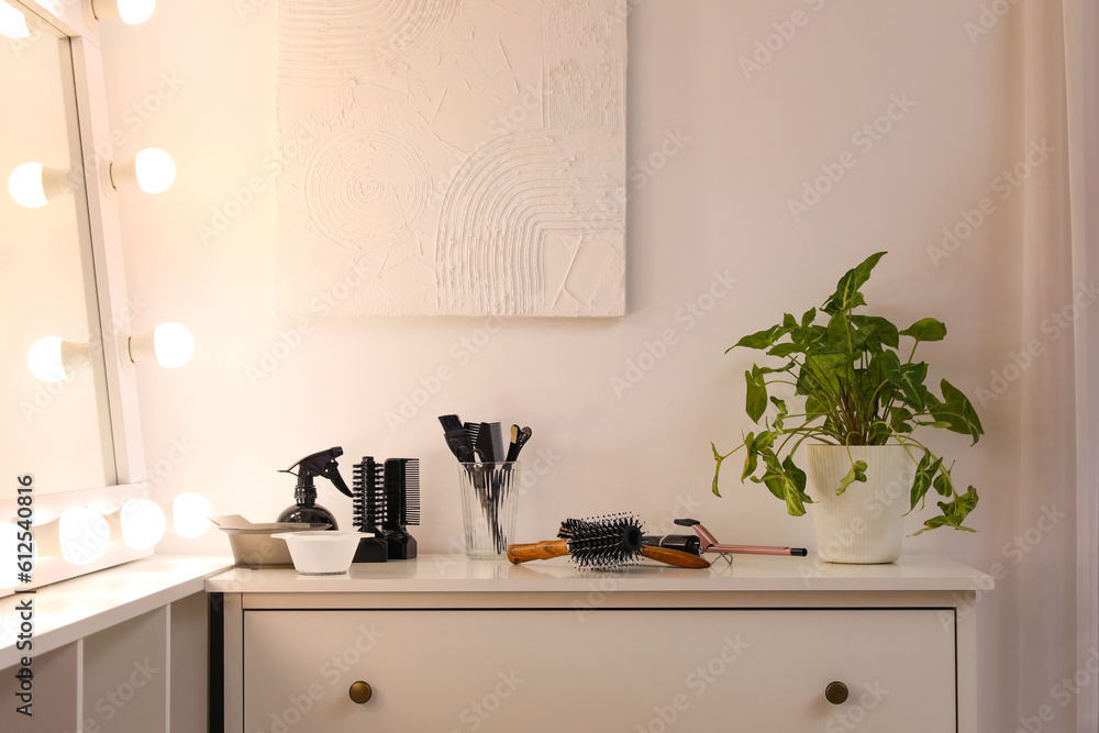 Different hairdressing tools on table near light wall