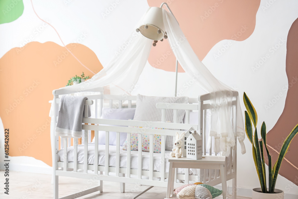 Interior of stylish bedroom with baby crib, lamp and stepladder